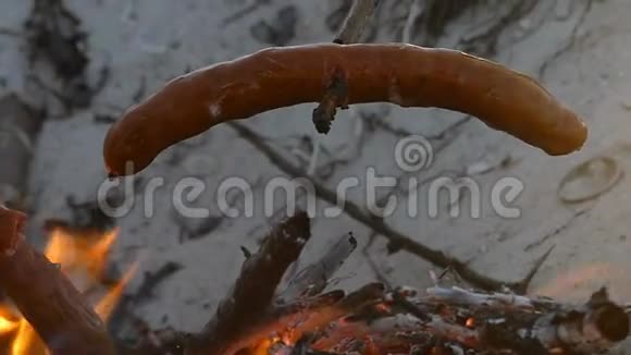 木棍上的两根香肠是在邋遢的篝火上煮的视频的预览图