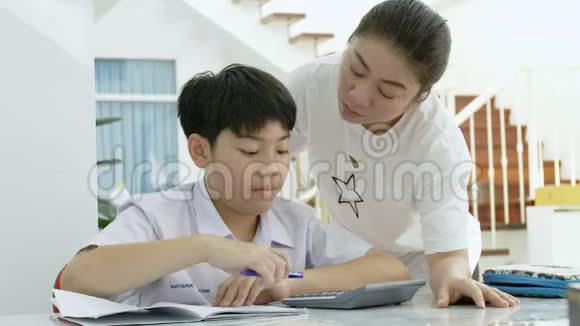 亚洲母亲的慢动作帮助她的儿子在白色桌子上做作业视频的预览图