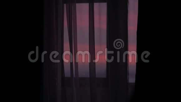 一个年轻人来到一扇窗前用夕阳关上窗帘的剪影视频的预览图