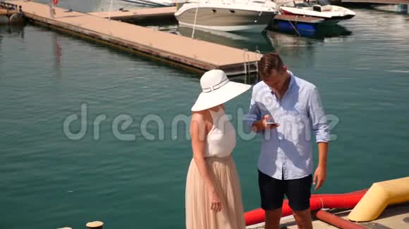 一对相爱的夫妇正和游艇站在码头上看着电话4K慢动作视频的预览图