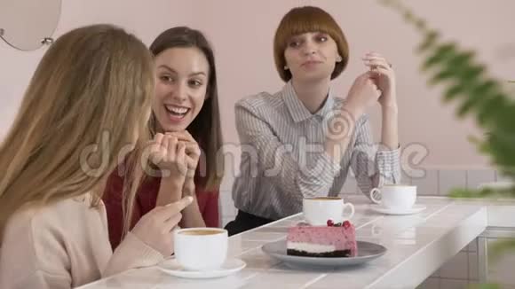 三个白种人年轻的女孩坐在咖啡馆里喝着咖啡吃着蛋糕微笑着笑着手势视频的预览图