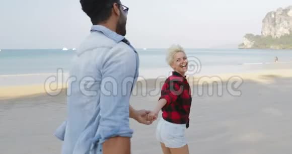 女人牵着男人的双手在沙滩上奔跑年轻的快乐游客在度假视频的预览图