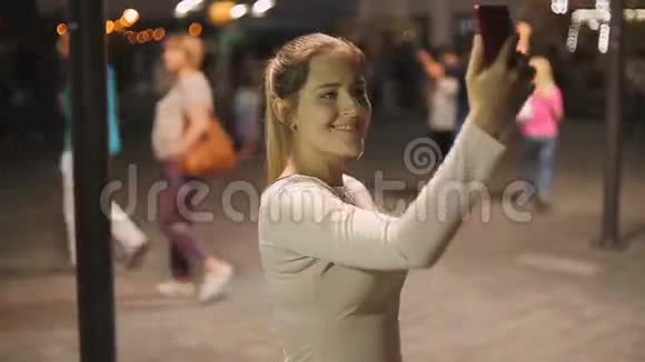 一幅优雅的年轻女子在拥挤的街道上晚上自拍的画像视频的预览图