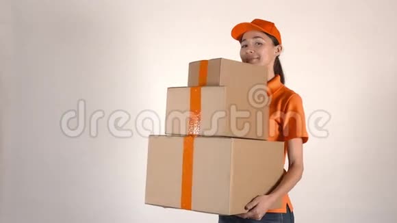 穿着橙色快递制服的漂亮女孩送了一叠纸箱浅灰色背景4K摄影棚拍摄视频的预览图