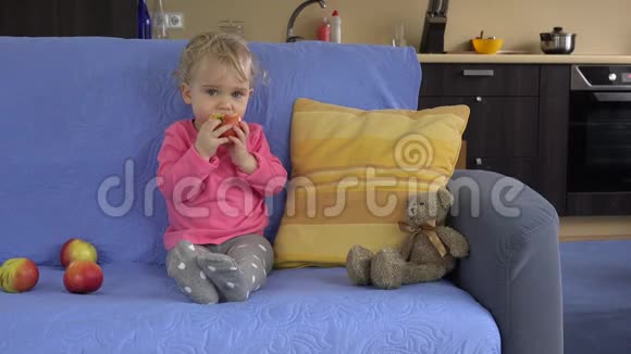 可爱的女婴坐在沙发上吃大苹果水果视频的预览图