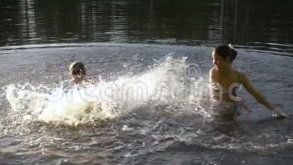 日落时分两个孩子在池塘里泼水的剪影视频的预览图