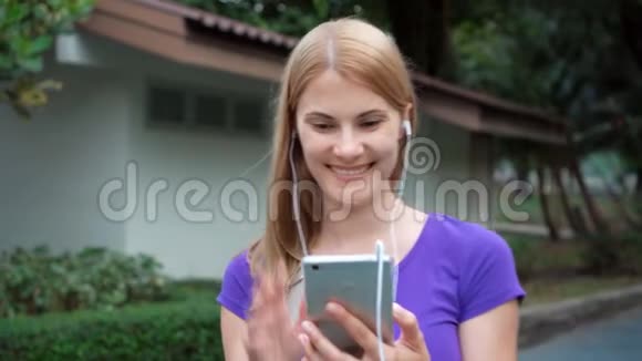 美丽的女孩走在公园里通过Skype与朋友用智能手机微笑交谈视频的预览图