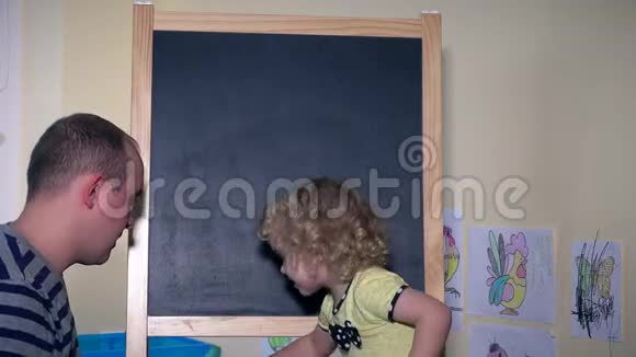 父亲带着他蹒跚学步的女儿孩子在黑板上学习字母视频的预览图
