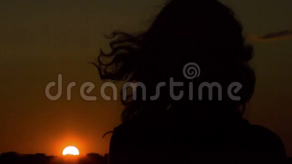 孤独的年轻女子看着夕阳想着风在吹她的头发视频的预览图