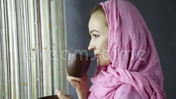 美丽的穆斯林阿拉伯妇女穿着粉红色头巾在窗前喝咖啡视频的预览图