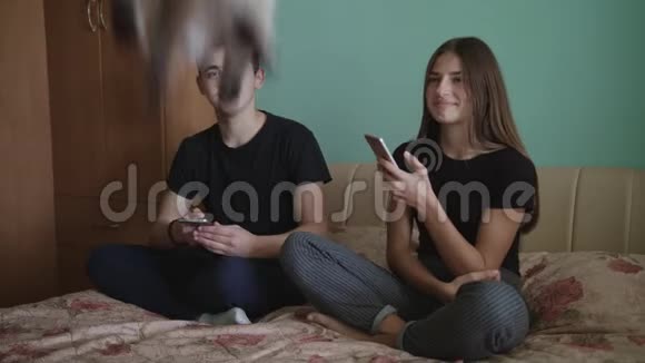 年轻人和漂亮的女孩坐在一个有蓝色墙壁的房间里玩手机视频的预览图