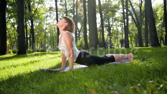 4K慢动作视频中老年微笑妇女在阳光明媚的夏日在公园练习瑜伽和冥想视频的预览图