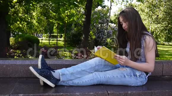 可爱的少女坐在公园的长凳上看书在户外学习高清视频静态画面拍摄视频的预览图