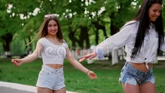 在公园的一个阳光明媚的日子里两个穿着短短裤的年轻女孩牵着手在赛格威骑车欢笑视频的预览图
