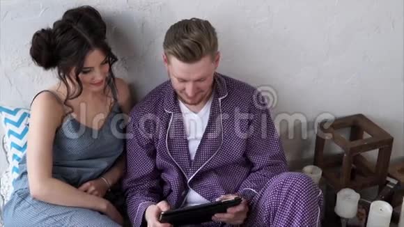 快乐的一对夫妇用他们的平板电脑在卧室的家里在线购买视频的预览图