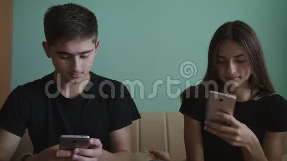 年轻人和漂亮的女孩坐在一个有蓝色墙壁的房间里玩手机视频的预览图