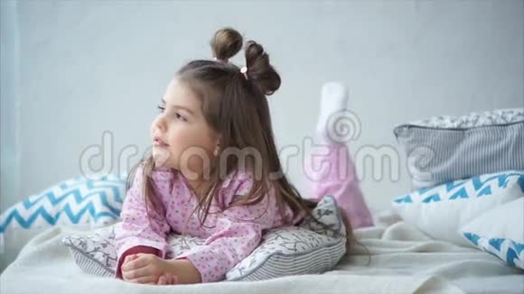 可爱快乐的小女孩穿着粉红色睡衣躺在床上枕头上视频的预览图