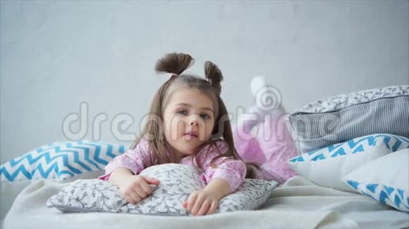 小女孩穿着可爱的睡衣躺在床上若有所思地抖着腿视频的预览图