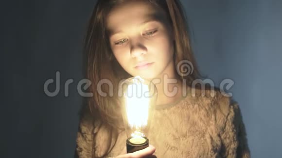 一个年轻女孩手里拿着一个发光的灯泡的特写肖像视频的预览图