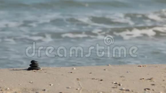 用黑色石头制成的金字塔矗立在沙滩上以海浪为背景视频的预览图
