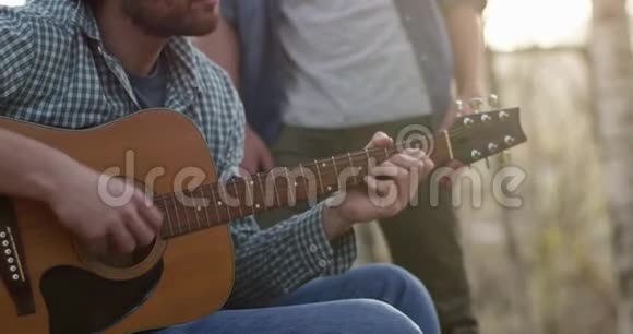 人们在火地附近用热饮料弹吉他放松真正的朋友户外露营帐篷视频的预览图