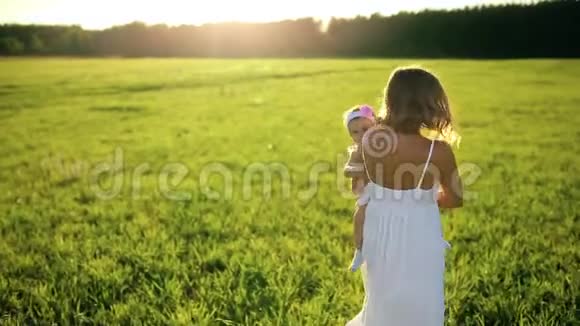 母亲带着女儿在日落时穿着白色的裙子穿过公园看着相机视频的预览图