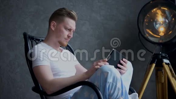 一个严肃的男人穿着睡衣紧张地看着平板电脑的屏幕视频的预览图