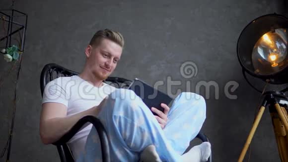一个穿着睡衣的好男人坐在椅子上看着小玩意上的照片视频的预览图