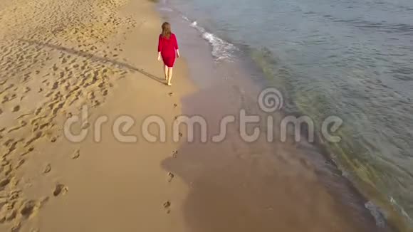 在潮湿的沙滩上赤脚行走的女人的后景海浪冲刷着沙滩上的脚印视频的预览图