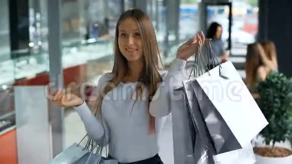 带着购物袋的年轻女人微笑着摆姿势背景中的商店灯视频的预览图