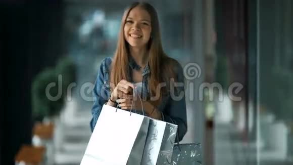 带着购物袋的年轻女人微笑着摆姿势背景中的商店灯视频的预览图