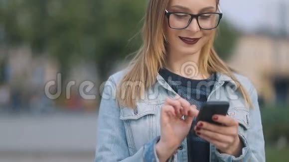 年轻快乐微笑的时髦女孩在户外使用现代智能手机在公园里通过手机发短信视频的预览图