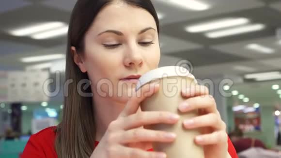 在食品场的快餐店里一个口渴的女孩从纸杯里喝咖啡视频的预览图