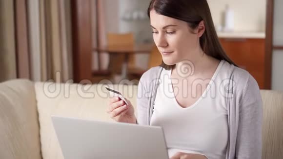 坐在客厅沙发上的女人用笔记本电脑上网买信用卡网上购买视频的预览图
