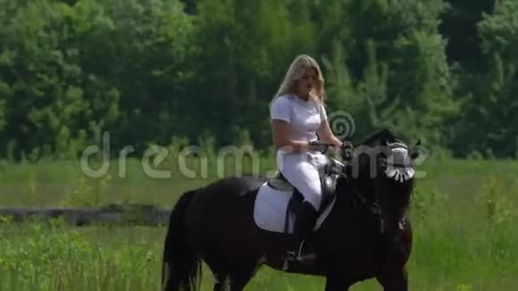 一个穿着白色头发和白色衣服的漂亮女孩慢慢地骑在赛马场的一匹黑色棕色种马上视频的预览图