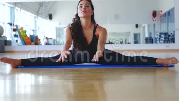 年轻的黑发女人在健身房里训练她在垫子上交叉分裂的灵活性视频的预览图