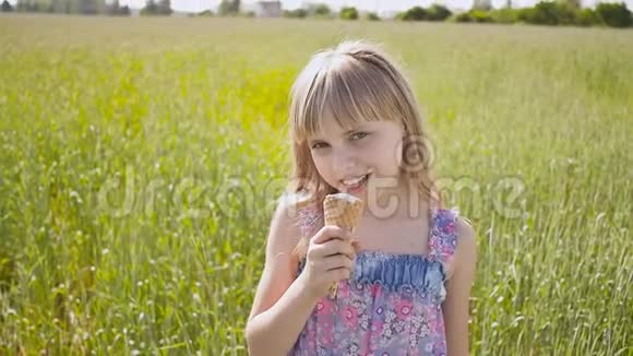 美丽的金发小女孩在麦田旁边吃冰淇淋温暖的晴天视频的预览图