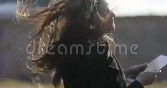 风在吹着年轻女孩的头发在春天的一天在外面的一个建筑工地上看着平板电脑视频的预览图