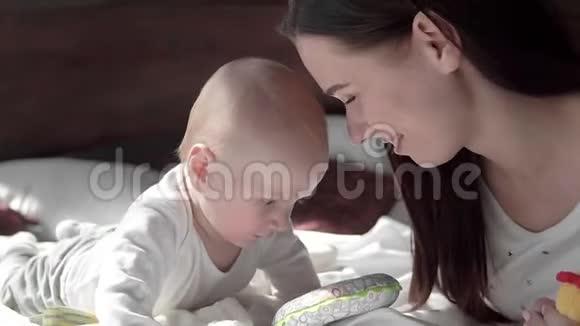 一位美丽的母亲和婴儿在床上微笑的特写肖像视频的预览图
