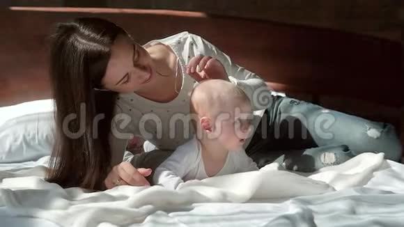一位美丽的母亲和婴儿在床上微笑的特写肖像视频的预览图
