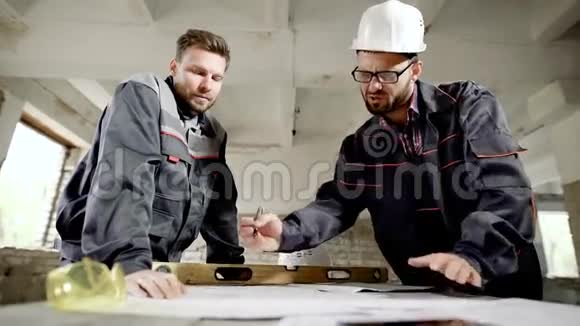 承包商和工人在餐桌上工作两个穿制服的男子正在为新项目制定计划视频的预览图
