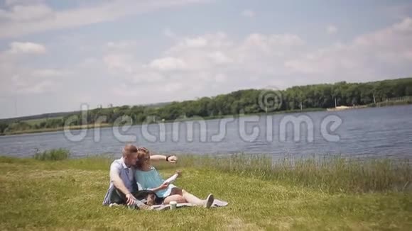 在河边的草地上约会恋爱的年轻夫妇一个男人和一个女孩和一只狗散步视频的预览图