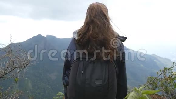 年轻的女游客背着背包在山上欣赏美丽的景色穿着雨衣的女旅行者站在视频的预览图