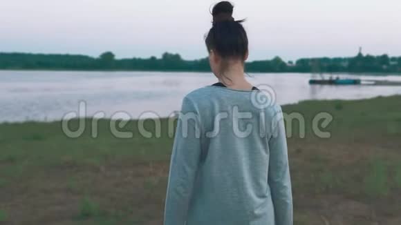 早上在海岸散步的年轻女子绿草如茵湖水夏季视频的预览图