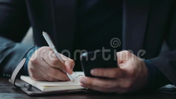 一个长着漂亮胡子的年轻商人用他的智能手机写着笔记看着相机和视频的预览图
