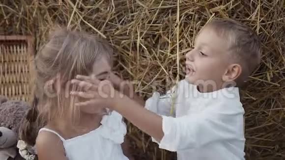 小快乐的孩子们雨后玩耍男孩带着一个女孩和一个黄色的田野带着一捆稻草视频的预览图