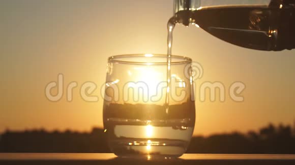在金色的傍晚阳光反射的背景下将矿泉水倒入玻璃中的慢速特写镜头视频的预览图
