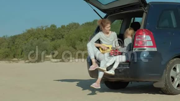 一个女人坐在海边的敞篷后备箱里的四弦琴上玩耍视频的预览图