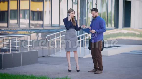 男人在同事打电话时签文件在女同事打电话时商人在文件上签名视频的预览图