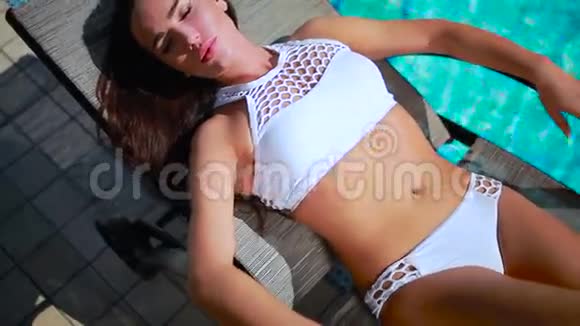 优雅的女人躺在游泳池附近的躺椅和日光浴上视频的预览图